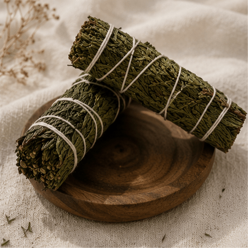 Two bundles of dried green herbs tied with white string, arranged on a round wooden plate over a beige linen surface.